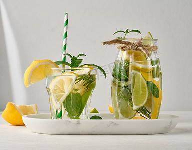 透明玻璃杯中的柠檬水，白色背景上有柠檬、酸橙、迷迭香小枝和薄荷叶