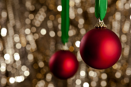 金色闪光摄影照片_金色闪光背景前的两个红色圣诞小饰品