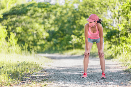 在跑步锻炼期间呼吸疲惫的活跃跑步女性戴着 COVID-19 面罩，在夏季炎热的户外越野跑中休息时筋疲力尽。
