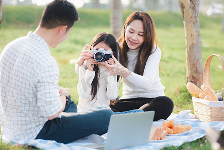 一家人的父亲、母亲和孩子一起玩乐，享受户外活动，坐在草地派对上拍照