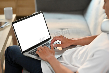 在明亮的客厅的沙发上休息的休闲男子在笔记本电脑上浏览互联网的特写视图