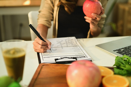 营养师拿着苹果，在办公桌前用新鲜水果写食谱。