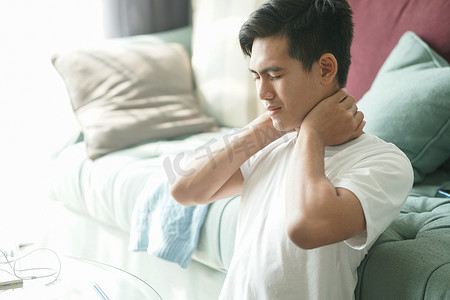 颈部疼痛摄影照片_疲惫不堪、沮丧的亚洲学生男性青少年企业家在家工作时颈部疼痛