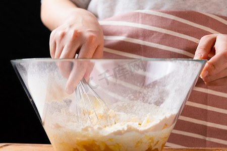 搅拌碗摄影照片_女面包师手在搅拌碗中揉面团的特写。