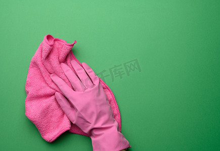 粉色橡胶手套中的女手拿着紫色背景上的粉色清洁抹布，特写