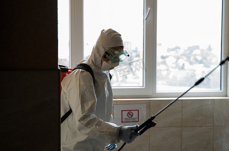 May摄影照片_UKRAINE, KYIV - May 20, 2020：身穿白色防护服和面具的男子正在对建筑物内表面进行消毒，同时冠状病毒流行以预防感染和控制流行病。