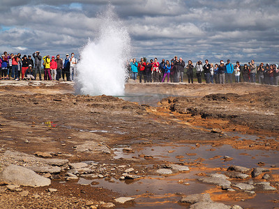 冰岛，STROKKUR，2016 年 7 月 26 日：Strokkur 间歇泉喷发黄金圈，一大群穿着五颜六色的游客拍照等待间歇泉喷发。 