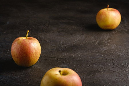 三鲜米粉摄影照片_深黑色纹理背景中鲜甜的三个苹果