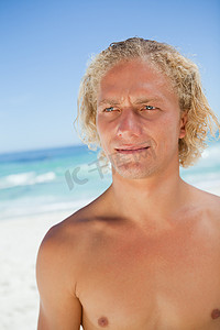 严肃的金发男人站在沙滩上看着侧面