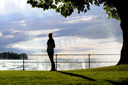 海边一位年轻女子站在草地上，身后溅起水花的剪影