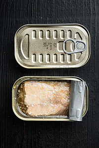 阿拉斯加三文鱼摄影照片_罐头野鳟鱼，锡罐，黑色木桌背景，顶视图平躺