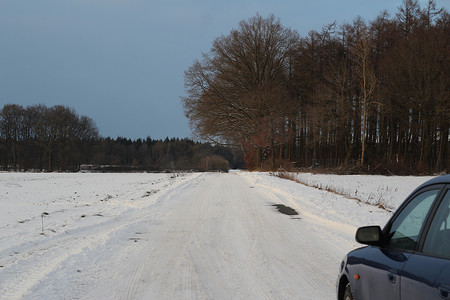 在多雪的土路上的蓝色汽车在田地旁边