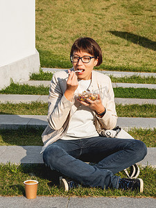女人坐在公园长椅上，带走午餐盒和纸板