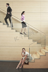 爬楼梯女摄影照片_年轻的女商人在与同事在办公室爬楼梯时使用手机时望向别处