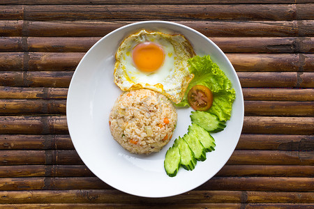 棕色竹桌上的白盘子里放着炒鸡蛋、米饭和新鲜蔬菜。