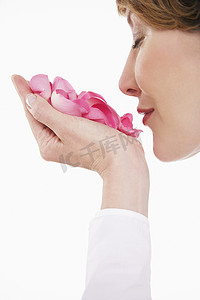 白色背景下手持粉红色玫瑰花瓣的女性特写侧视图