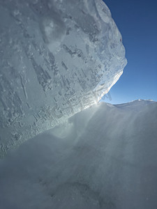 蓝色结晶摄影照片_阳光明媚的冬日冰坡，蓝色透明的冰，纯蓝的天空，长长的阴影，纯净的积雪覆盖的处女地，雪地，
