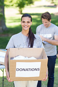捐款箱摄影照片_快乐的黑发志愿者拿着捐款箱