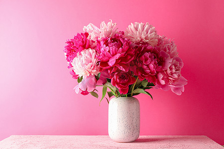花瓶，在粉红色的桌子上放着一束美丽的牡丹，背景是彩色的，文字空间