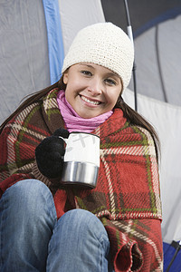 一位快乐的年轻女性拿着咖啡杯裹着毯子的画像