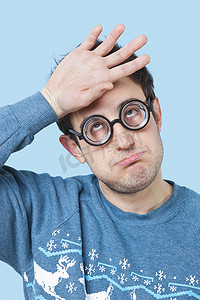 极客年轻人戴着新奇的眼镜，手放在蓝色背景上