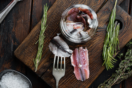 罐装鳀鱼，在木制切菜板上，在旧的深色木桌背景上。