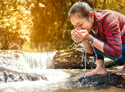女人在瀑布的杯状手中接住流动的纯净水