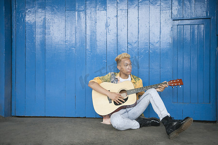 坐在木镶板墙上弹吉他的时髦少年