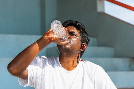 运动跑步者黑人戴着运动员耳机，在户外街道健康公园跑步后从瓶子里喝水