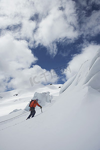 一名男性徒步者顶着云爬上雪山斜坡的侧视图