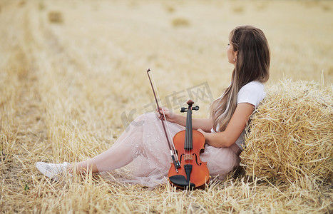 浪漫的年轻女人，头发飘逸，手里拿着小提琴，在田野里
