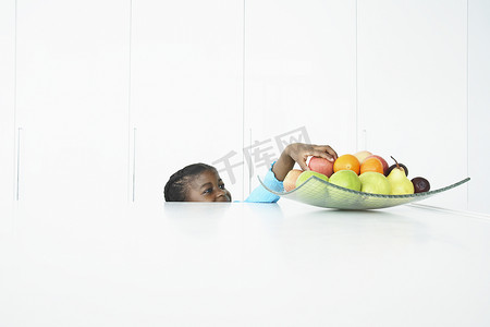 桌子后面的女孩试图拿到桌上盘子里的水果
