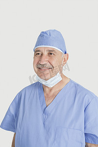 灰色背景中带手术面罩和帽子的快乐高级男外科医生