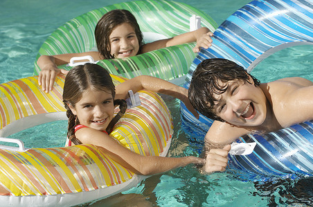 胡闹摄影照片_三个嬉戏的兄弟姐妹在游泳池里玩充气筏的肖像