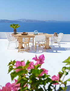 露台餐厅摄影照片_希腊圣托里尼海边一家餐厅的户外露台，海边的椅子和桌子上放着鲜花