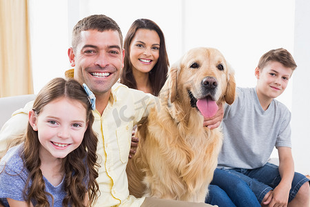 微笑的家人和金毛猎犬坐在沙发上