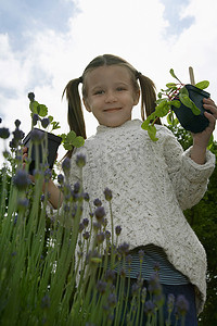 儿童培育摄影照片_一个小女孩在花园里对着天空拿着植物的低角度肖像