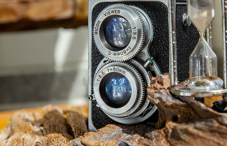 相机焦距摄影照片_木制背景上带沙漏的老式双镜头相机