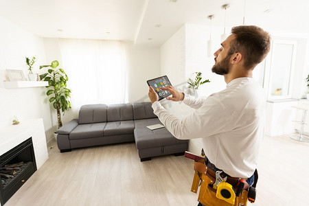 维修、施工和建筑概念-快乐微笑的工人或生成器与 tablet pc 计算机和工具在家庭房间背景。