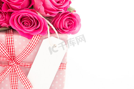 一束粉色玫瑰的特写，旁边是一件粉色礼物，白色背景上有一张空白卡片