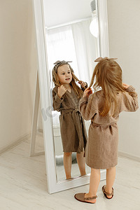 一个穿棕色外套的女孩透过大镜子看着镜头