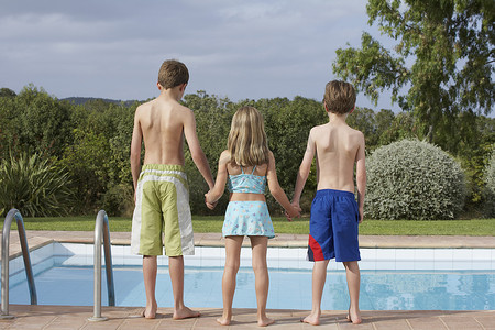 两兄弟和一个姐妹在泳池边的全长后视图