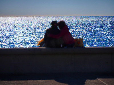 剪影拥抱摄影照片_从坐在海边的后面看到无法辨认的拥抱恋人的模糊图像
