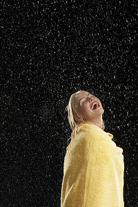 一个在雨中裹着黄色毛巾的笑着的年轻女人的侧视图