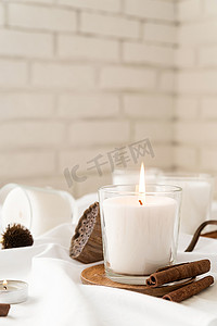 白色织物背景上带有肉桂和干花的美丽燃烧蜡烛