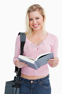 快乐的金发女人拿着一本小说和她的肩包