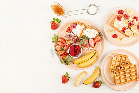 盘子里面放水果摄影照片_白桌上的盘子里放着自制的华夫饼，里面有水果和浆果、奶油和蜂蜜。
