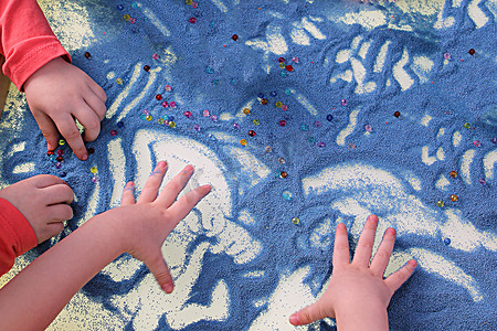 技能发展摄影照片_儿童手在白桌沙疗上触摸蓝沙，发展精细运动技能