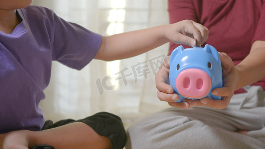 学龄前儿童男孩将零花钱硬币放入蓝脸小猪槽