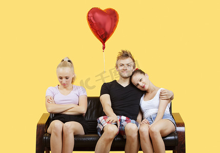 被环绕的心摄影照片_年轻夫妇坐在沙发上的肖像，女性朋友在黄色背景中感觉被冷落